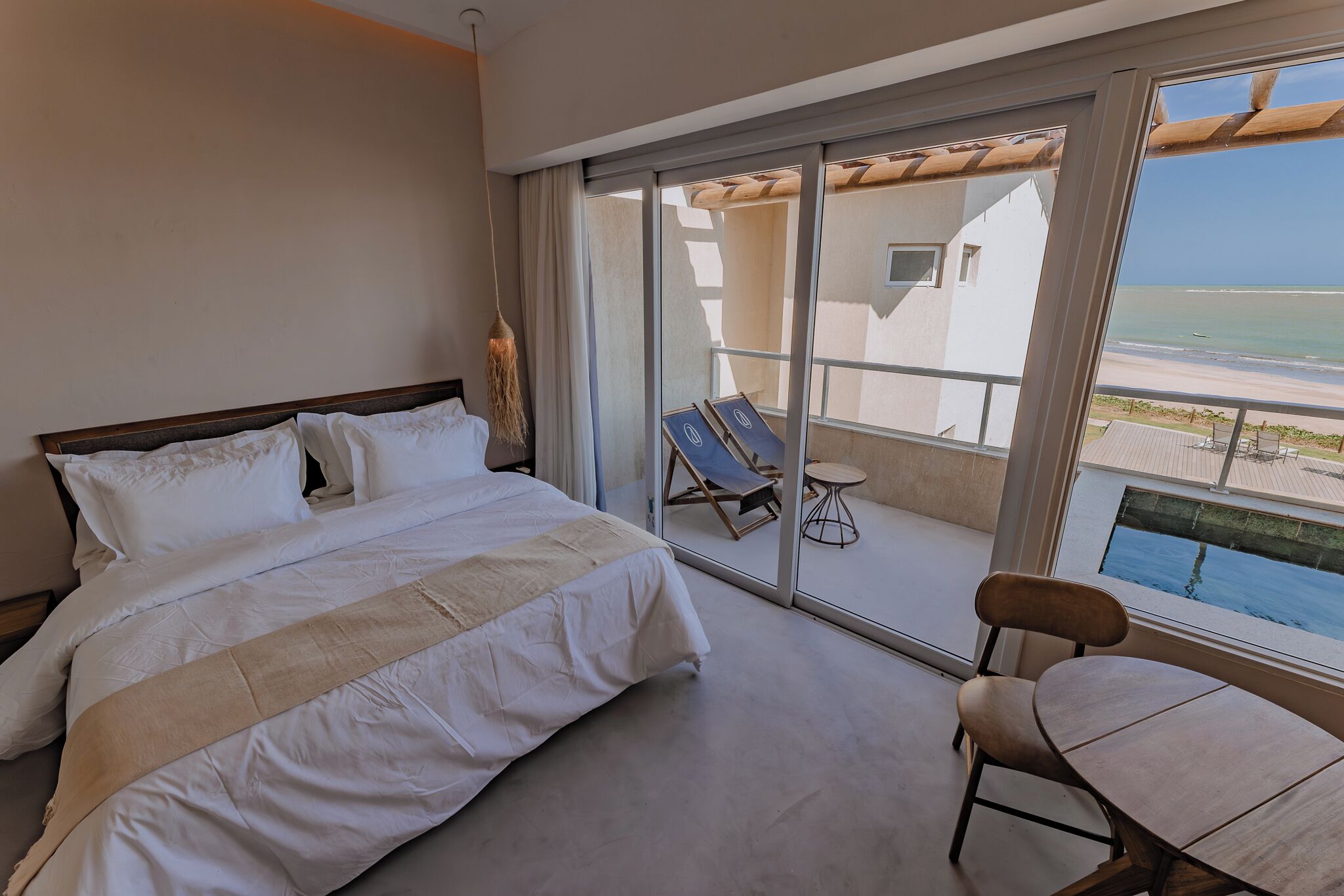 Ein Hotelzimmer mit einem Bett, einem Sessel und Meerblick durch große Schiebeglastüren.
