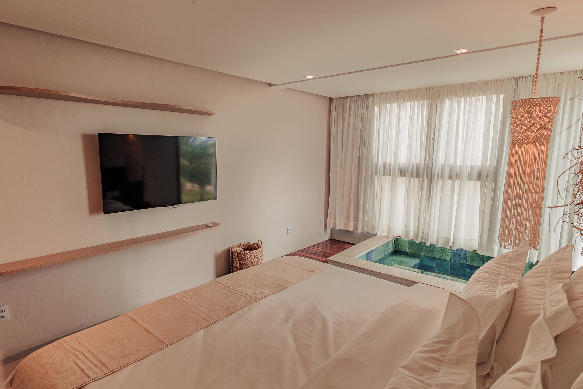 A modern bedroom with a large bed, a TV mounted on the wall, and a view of a swimming pool through sheer curtains.