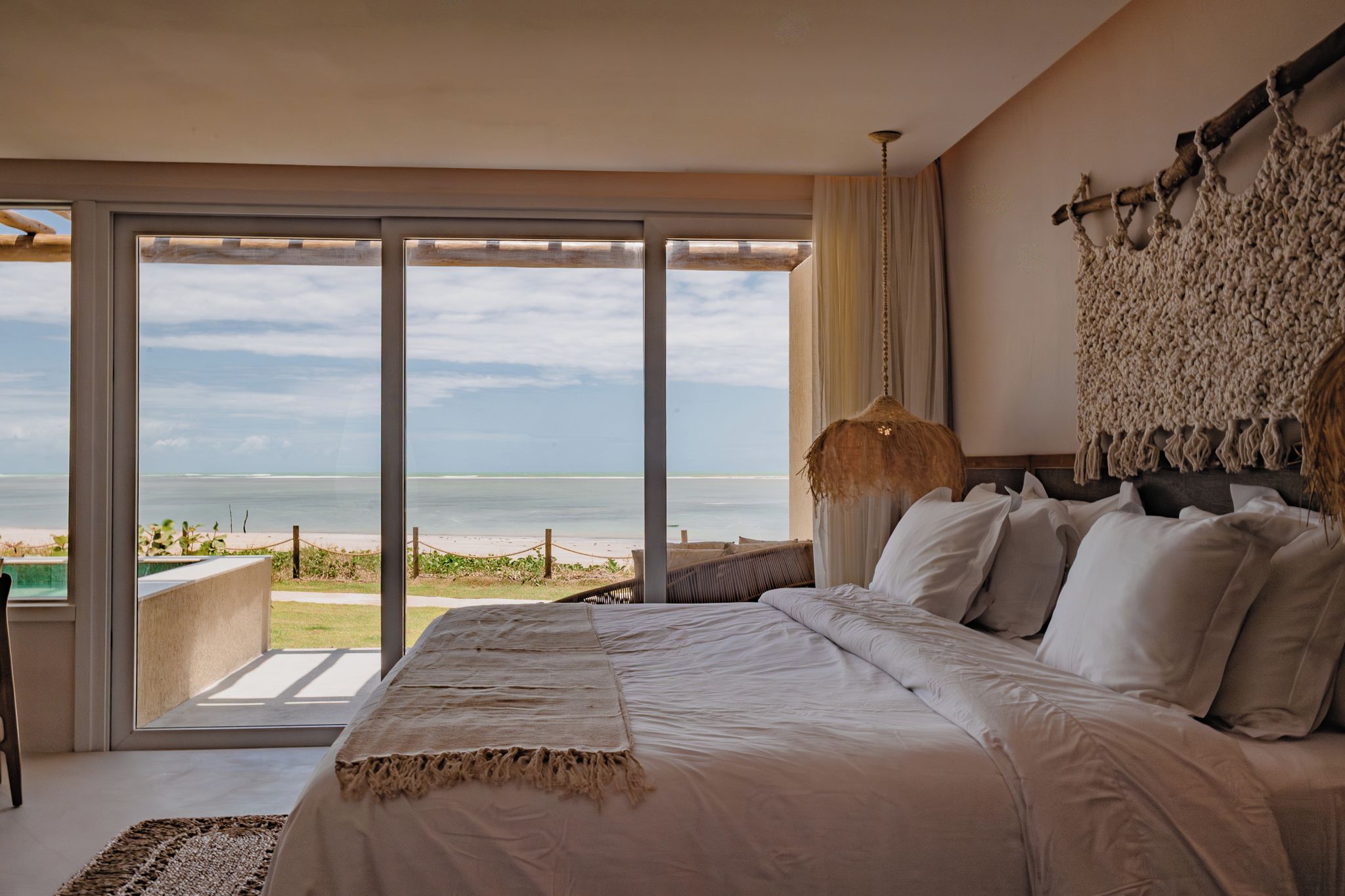 A bedroom with a large bed, a view of the beach, and a hanging light fixture.