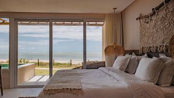 A bedroom with a large bed, a view of the beach, and a hanging light fixture.