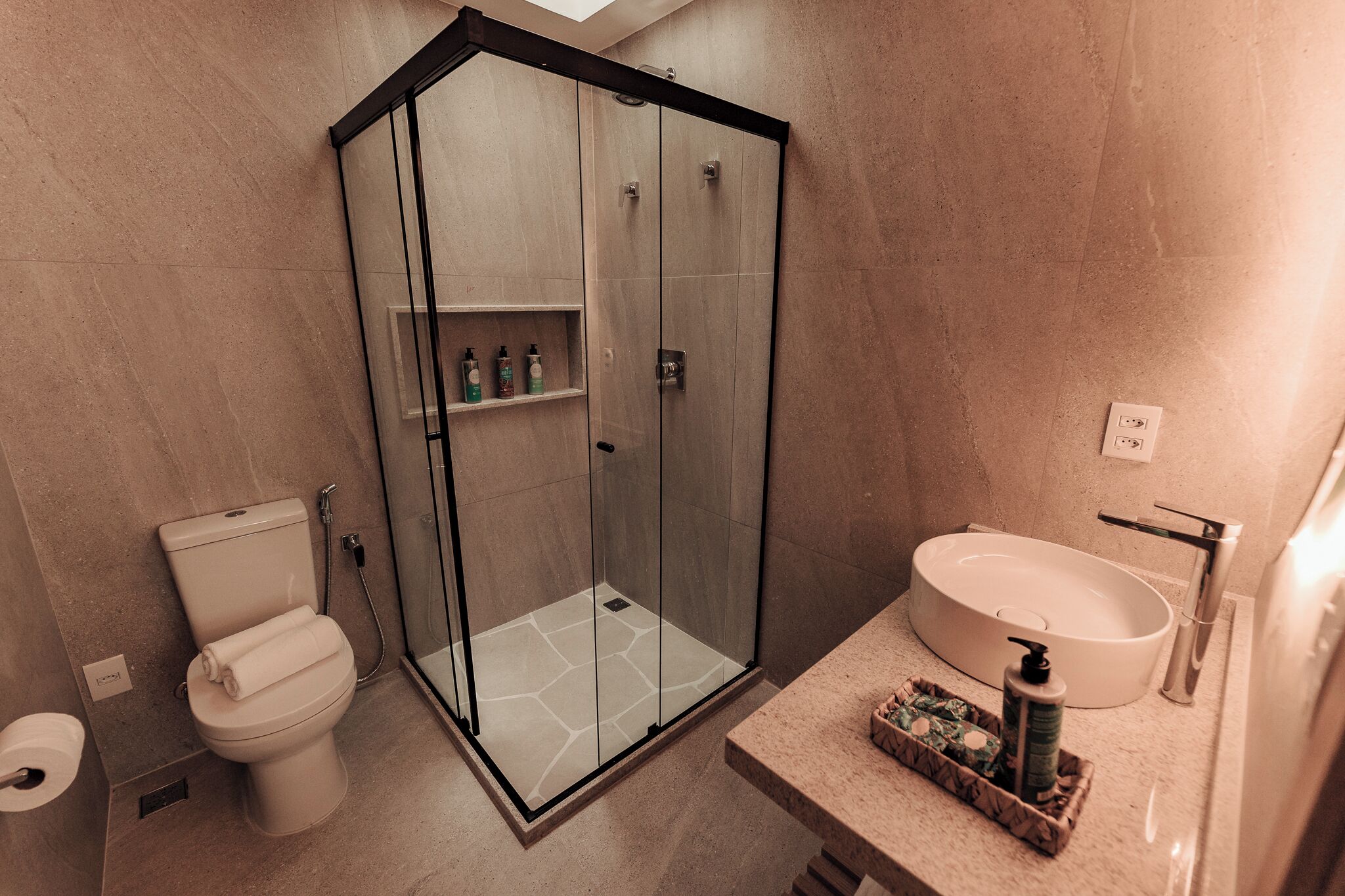 A modern bathroom with a glass-enclosed shower, a toilet, and a sink with a marble countertop.