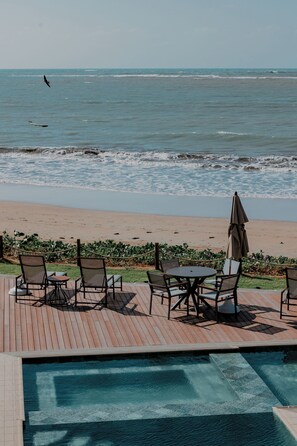 A poolside area with chairs and an umbrella overlooking the ocean. - Pousada Aysú (Japaratinga)
