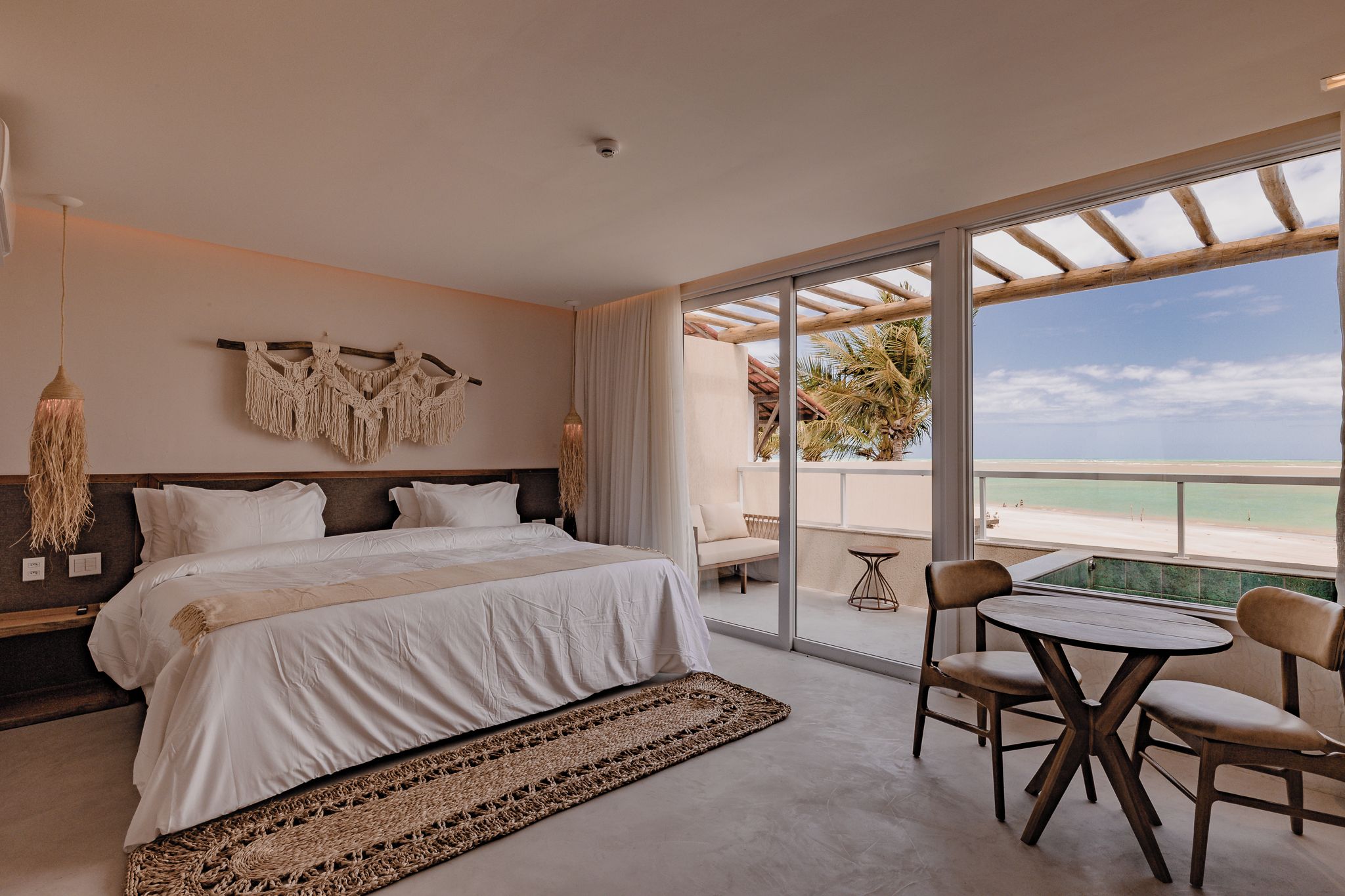 Un dormitorio con una cama grande, vistas a la playa y un balcón con mesa y sillas.