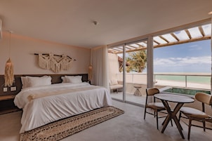 Un dormitorio con una cama grande, vistas a la playa y un balcón con mesa y sillas.