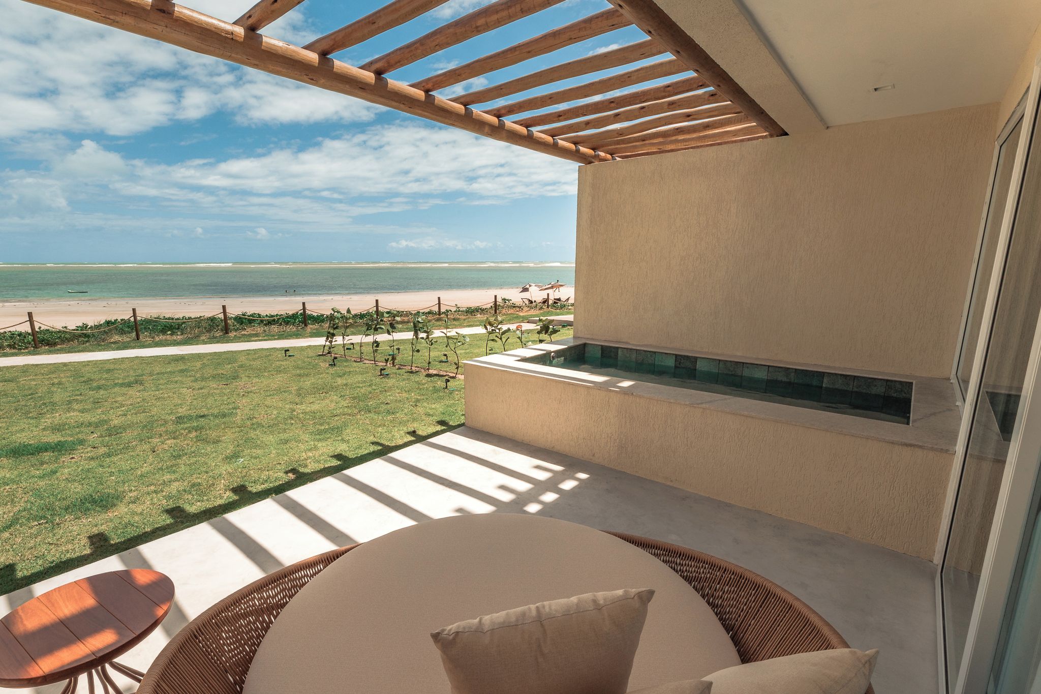 A balcony with a view of the beach, a seating area with a table and chairs, and a built-in water feature.