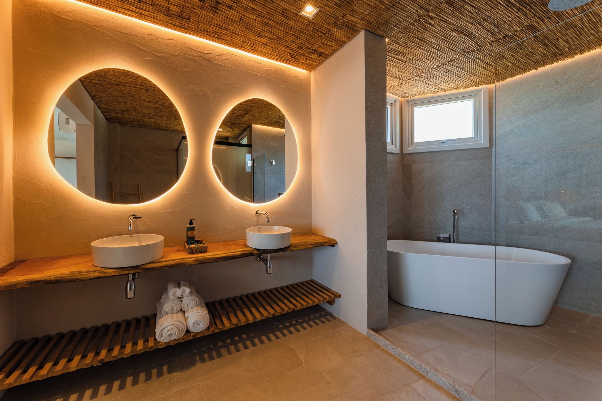 A modern bathroom with two sinks, a freestanding bathtub, and circular mirrors.