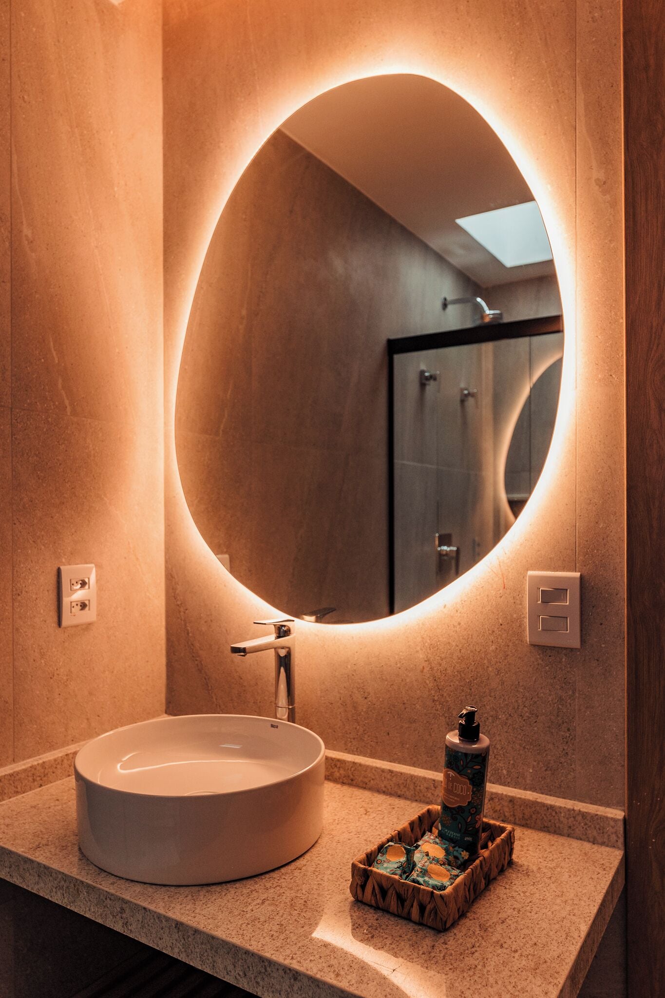 A bathroom with a round mirror, a sink, and a bottle of hand soap on the counter.