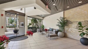En rummelig lobby med et moderne design, der inkluderer et siddeområde med sofaer og et sofabord, et stort vægmaleri samt potteplanter.