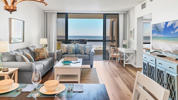 En moderne stue med sofa, sofabord og spiseområde. Et stort vindue med havudsigt.