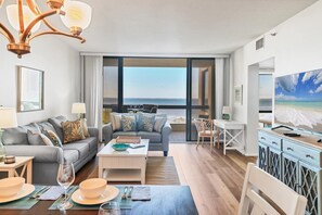 Ein modernes Wohnzimmer mit einer Couch, einem Couchtisch und einem Essbereich. Ein großes Fenster bietet Blick auf das Meer.