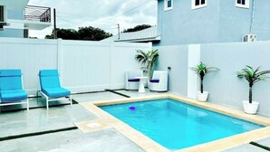 A rectangular swimming pool with a tiled deck, surrounded by a white fence. There are two blue lounge chairs and two white lounge chairs with blue cushions. - Private pool island retreat.

 (Nassau)