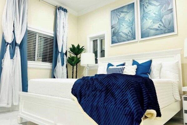 A bedroom with a white bed, blue bedding, and a window with curtains. - Private pool island retreat.

 (Nassau)