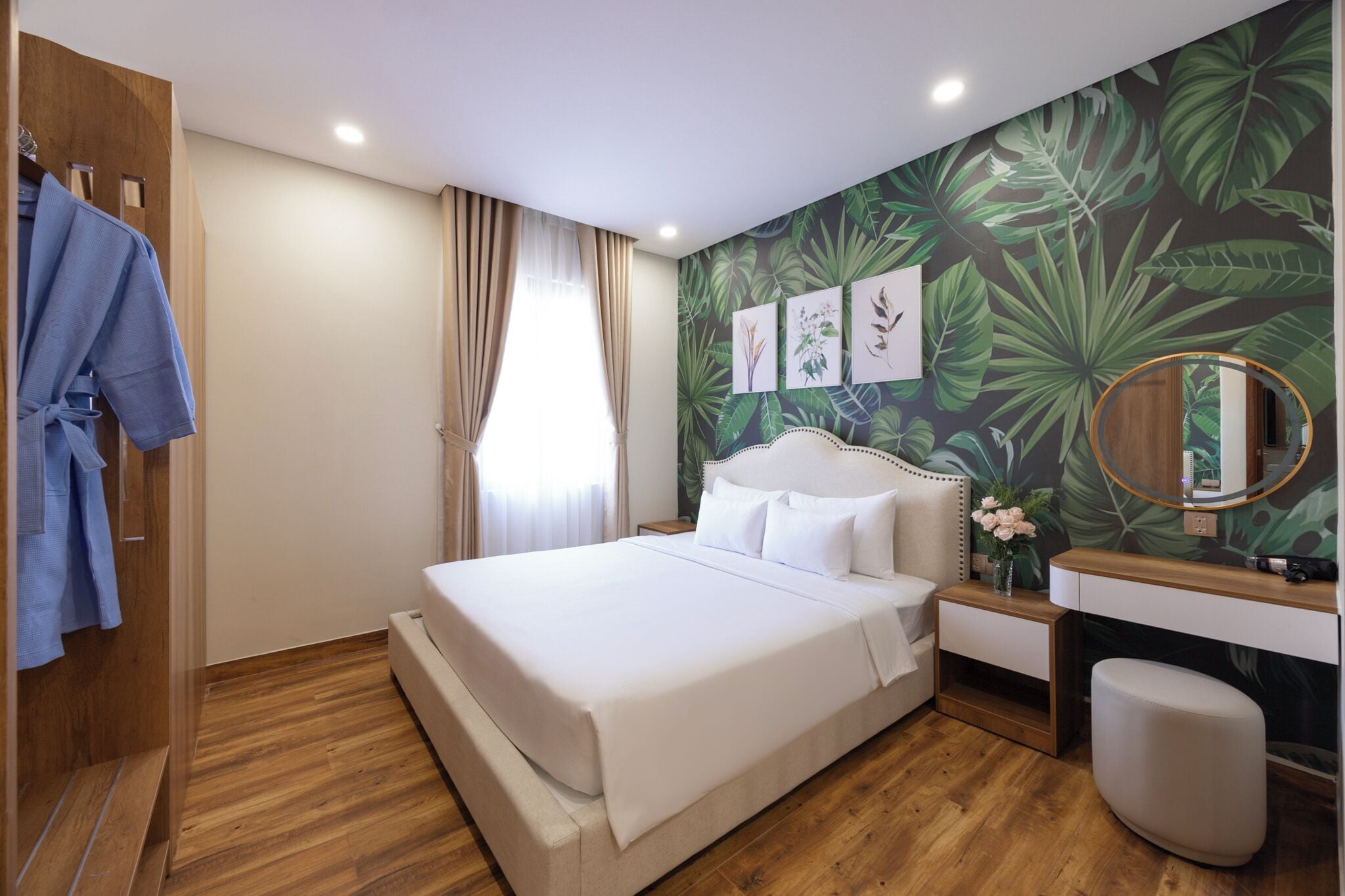 A hotel room with a large bed, a wooden wardrobe, a vanity with a mirror, and a tropical leaf-patterned wall.