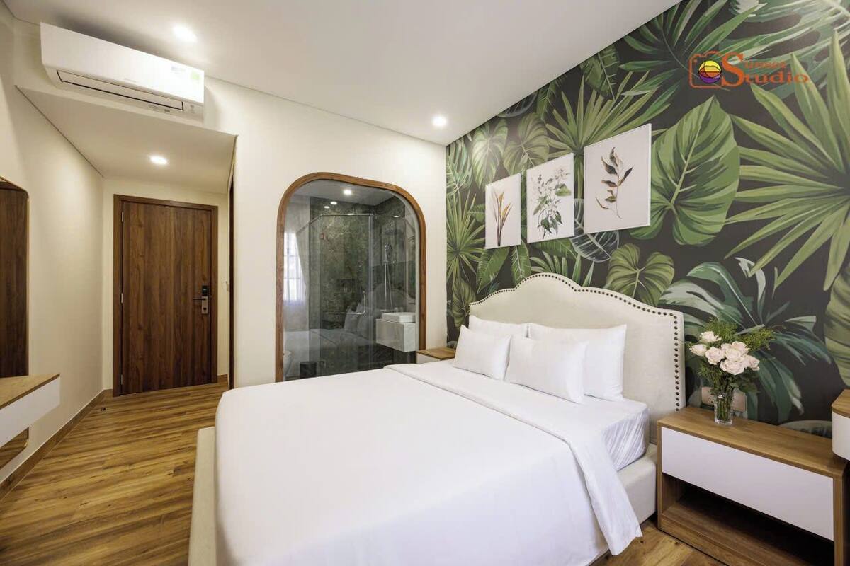 Ein Hotelzimmer mit einem großen Bett, Holzboden, einer Duschkabine und einer Wand im tropischen Stil.