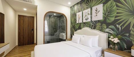A hotel room with a large bed, a wooden floor, a shower area, and a tropical-themed wall.