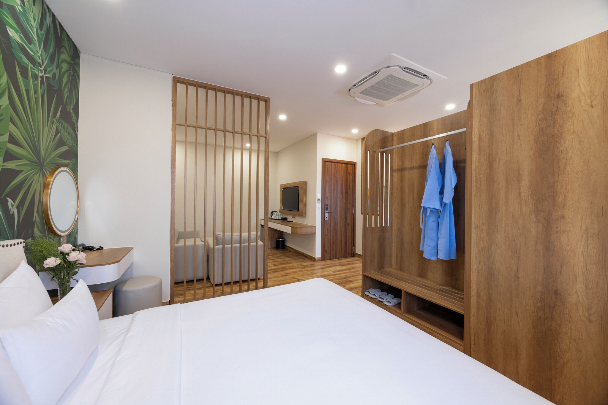 A modern hotel room with a large bed, a wooden wardrobe, a vanity with a mirror, and a desk with a chair.