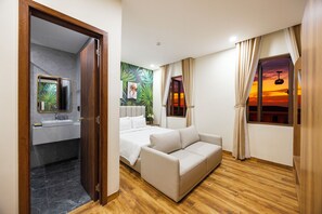 A hotel room with a wooden floor, a bed, a sofa, a bathroom with a sink, and a mural of tropical leaves. - Sarah Hotel and Halal Restaurant Phu Quoc (Phu Quoc)