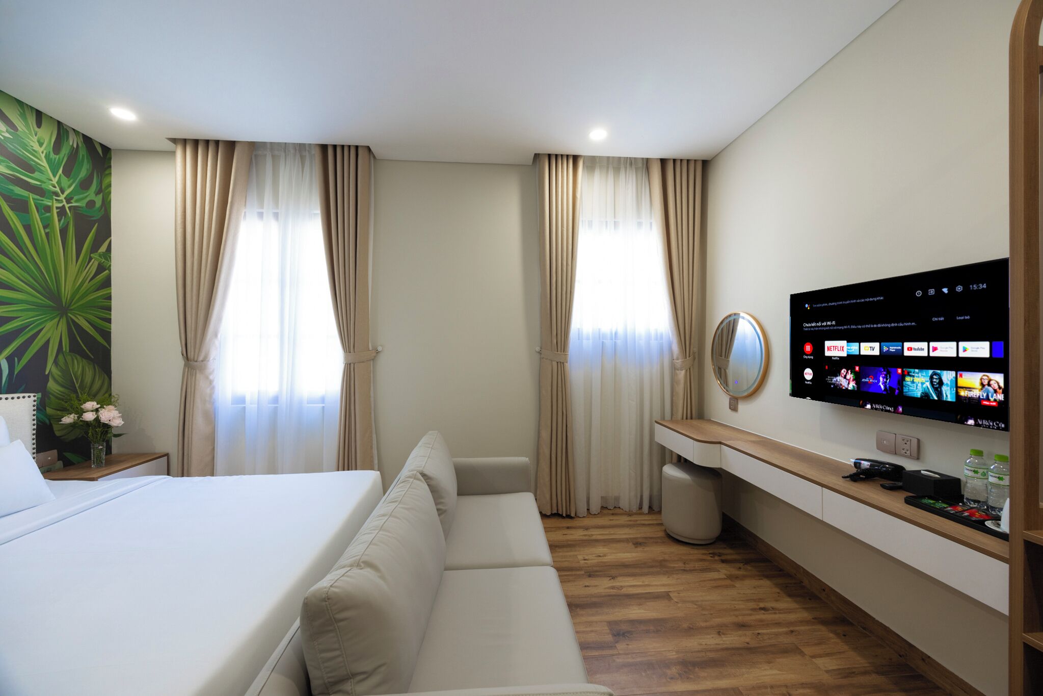 Une chambre d’hôtel avec un lit, un canapé, un téléviseur fixé au mur et un plancher en bois.