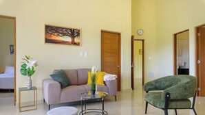 A living room with a sofa, a round coffee table, a green armchair, and a painting of a tree on the wall. - Casa Vista Mar 3 (Rio San Juan)
