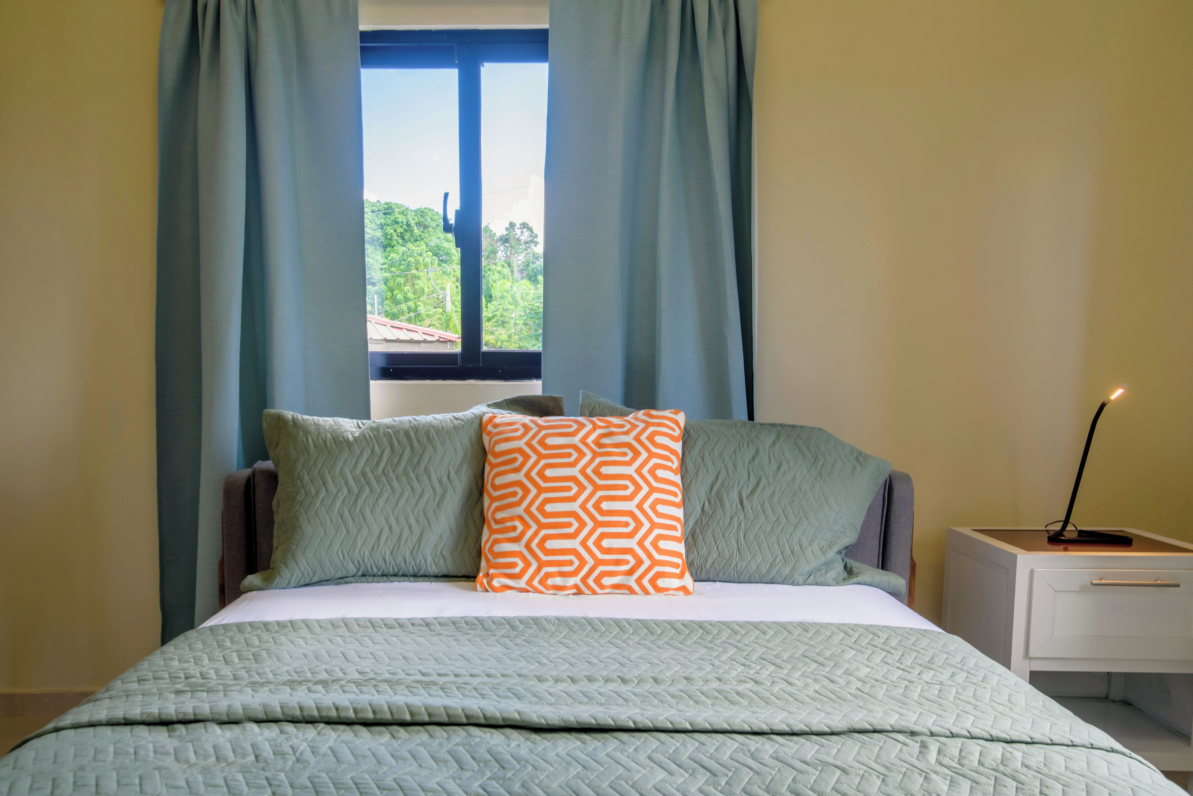 A bedroom with a bed, curtains, a window, and a bedside table.