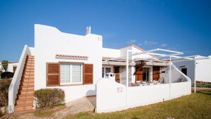 A modern white building with a staircase, a window with wooden shutters, and a covered outdoor seating area.
