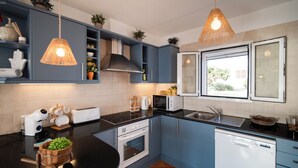 Una cocina moderna con armarios azules, encimera negra, horno empotrado, lavavajillas y lámparas colgantes.