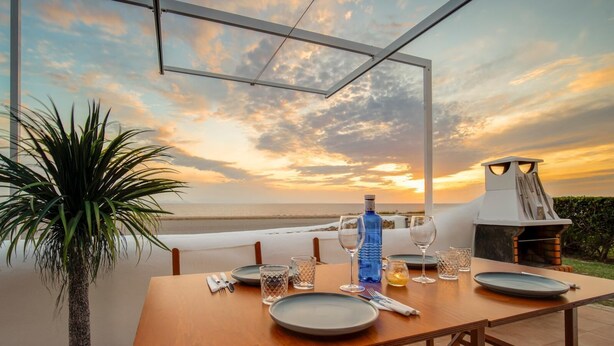 A dining table set for two with a view of the ocean at sunset.