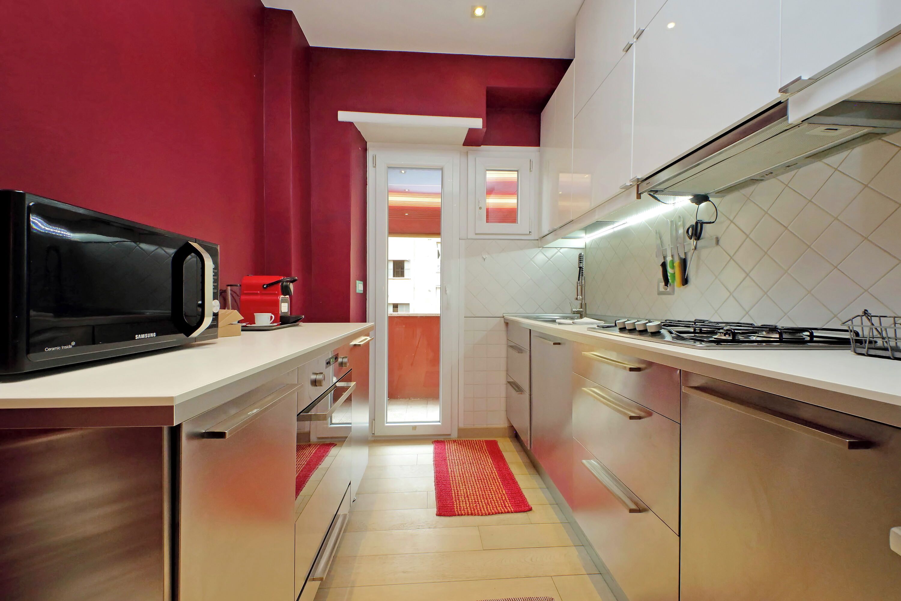 Una cucina moderna con elettrodomestici in acciaio inossidabile, mobili bianchi e una parete decorata in rosso.