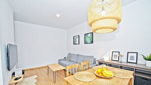 Un espacio habitable moderno con un sofá, una mesa de comedor con individuales tejidos, un televisor y obras de arte enmarcadas en la pared.