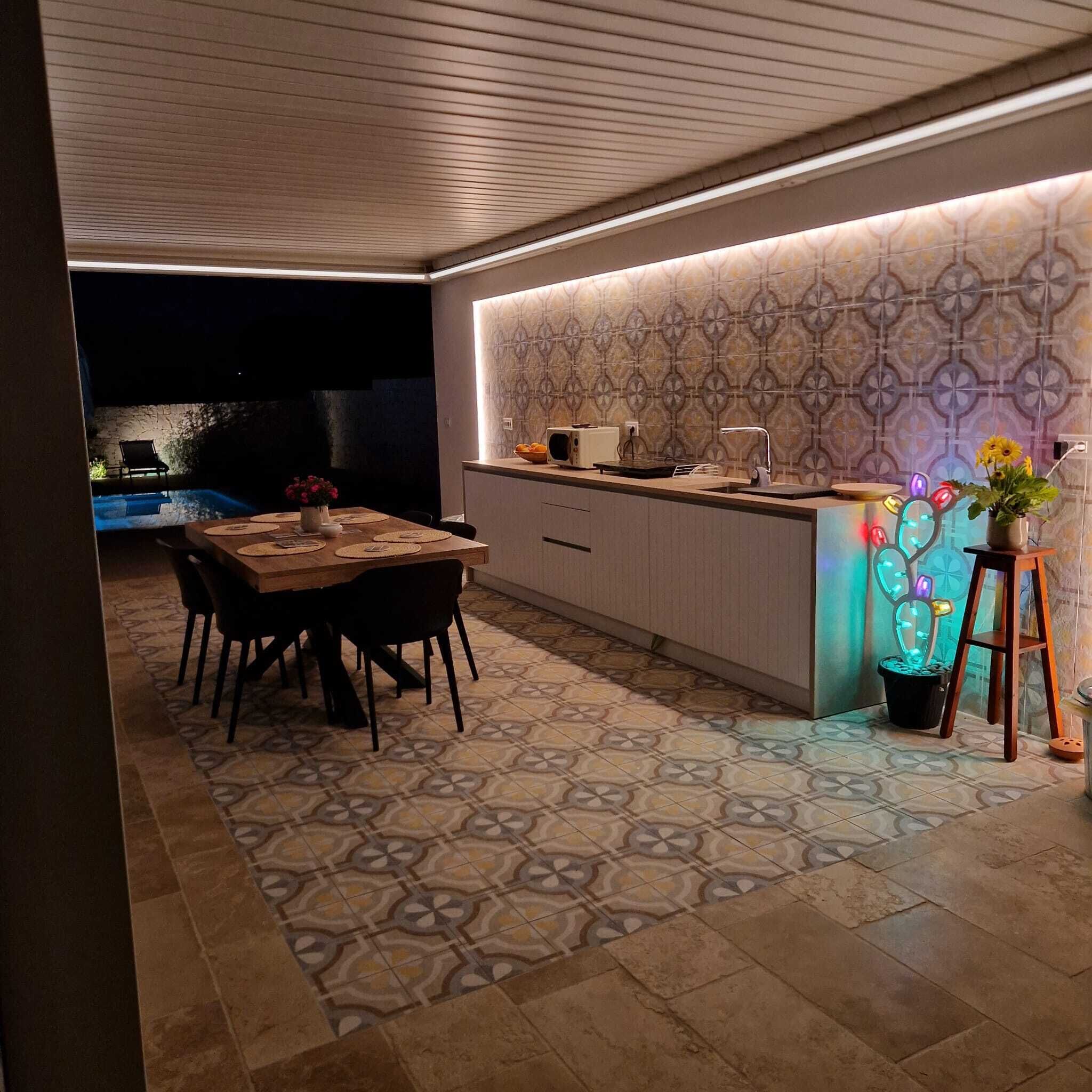 Une cuisine moderne avec un mur de crédence à motifs, un coin repas avec une table et des chaises, et une petite piscine en arrière-plan.
