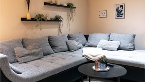 Un salon moderne avec un canapé d’angle gris, une petite table basse ronde et des étagères décoratives murales.