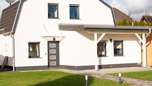 Une maison moderne à deux étages, avec une façade blanche, un toit foncé et une antenne parabolique sur le toit.