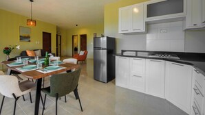 A modern kitchen with white cabinets, a stainless steel refrigerator, and a dining area with a wooden table and chairs. - Casa Vista Mar 4 (Rio San Juan)