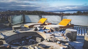 A rooftop terrace with lounge chairs, a fire pit, and a view of the surrounding landscape.