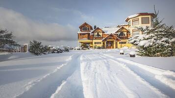 A large, multi-story wooden house with a snow-covered driveway and surrounding trees.
