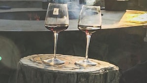 Two wine glasses on a wooden stump with a chef in the background.