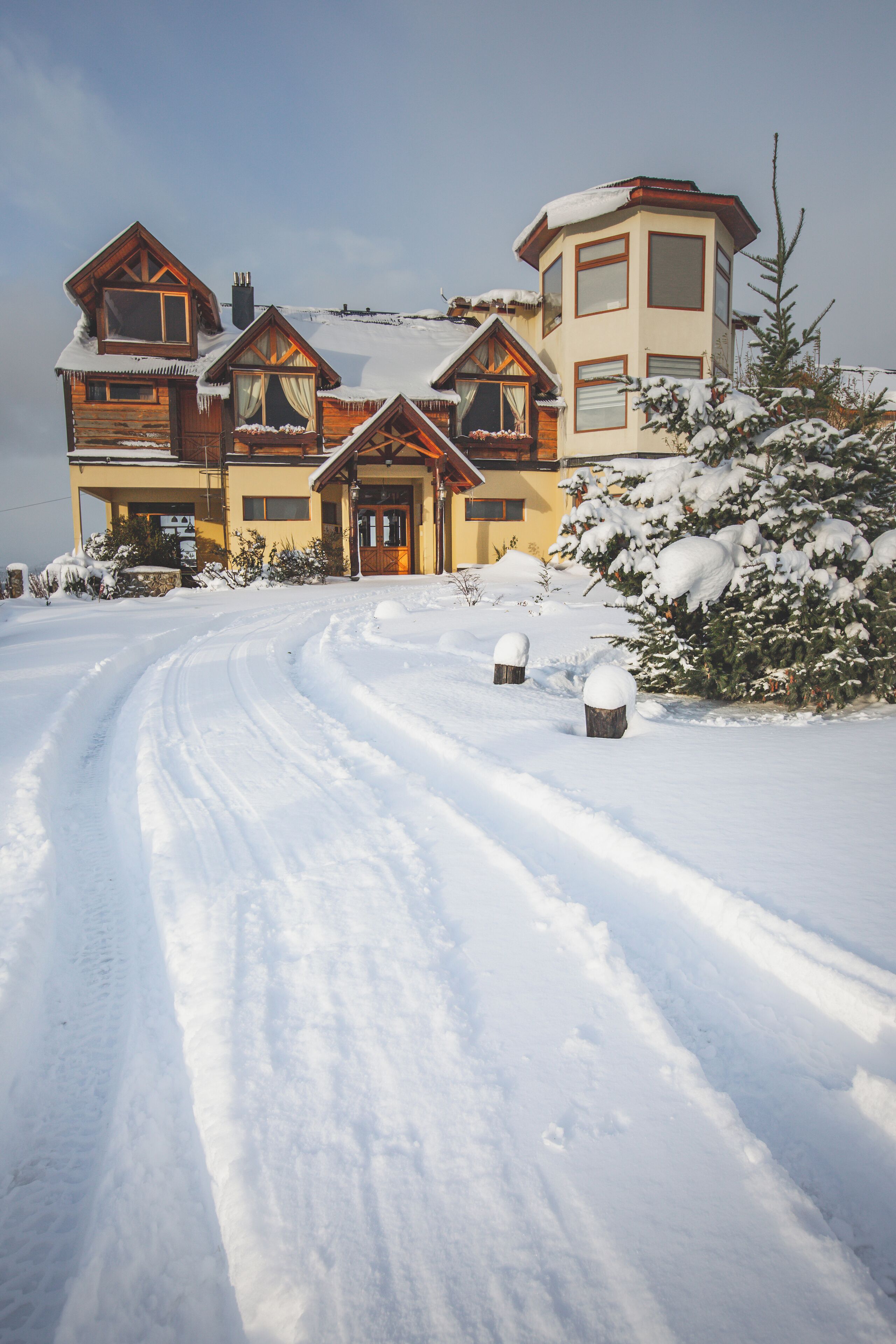 A snow-covered road leading to a chalet-style house with multiple wooden structures and a large central building.