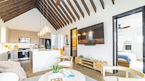 Un espai modern d'estar amb cuina, zona de menjador i un dormitori amb un televisor gran.