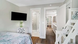 Een slaapkamer met een bed, een aan de muur bevestigde televisie, een witte dressoir en een witte stoel.