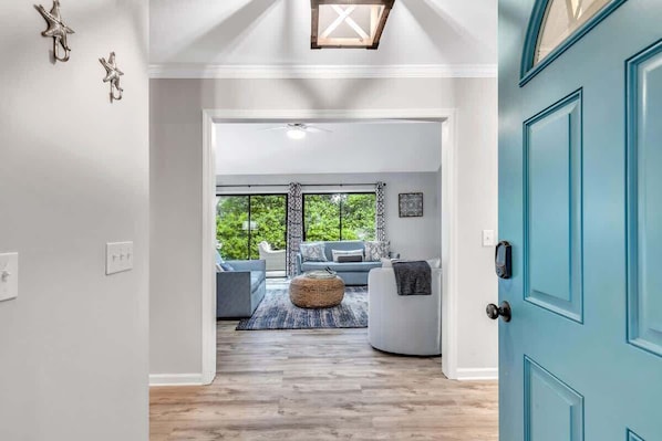 Un intérieur moderne avec une porte de couleur turquoise, un ventilateur de plafond et une vue dégagée sur l’extérieur grâce à une grande fenêtre.
