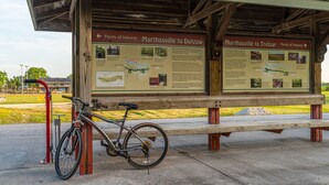 Un panel informativo de madera con mapas y texto, una bicicleta y un banco.