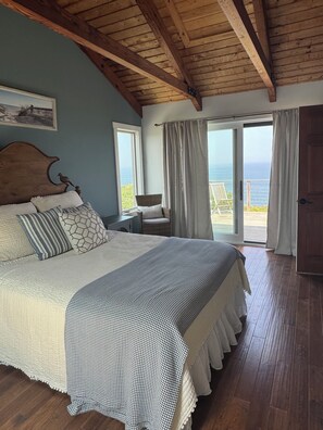 Une chambre avec un grand lit, un plafond en bois, une vue sur l’océan et un balcon équipé d’une chaise.