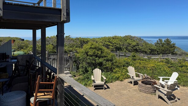 Terraza de madera con sillas Adirondack y un hogar para fuego con vistas panorámicas del océano y las colinas.