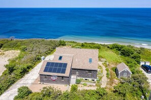 A building with solar panels, a small adjacent structure, and a view of the ocean. - Charming Handicapped Accessible 3-bedroom house in Welcoming Wellfleet (Wellfleet)