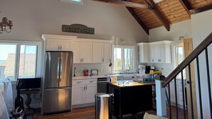 A spacious kitchen with white cabinets, a stainless steel refrigerator, and a wooden ceiling.