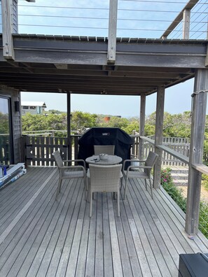 Une terrasse en bois dotée d’un espace salon couvert, d’un barbecue et offrant une vue sur un bâtiment situé au loin.