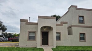 A two-story building with a flat roof, a central entrance with an arch, and a small porch area.