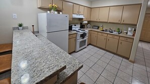 A kitchen with granite countertops, a refrigerator, a stove, and beige cabinets.