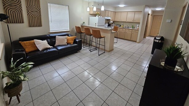 A modern kitchen with a central island, a dining area with bar stools, and a living room with a black leather sofa.