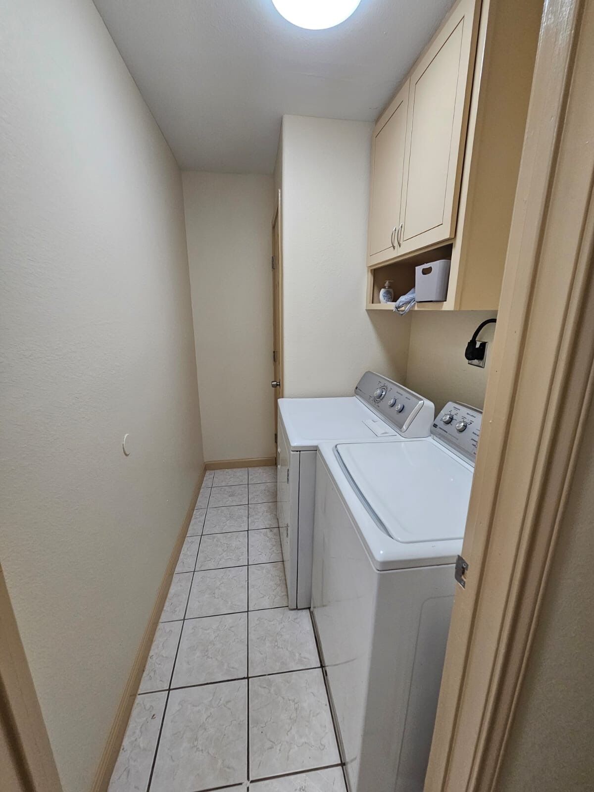 A laundry room with a washing machine and dryer, a tiled floor, and a ceiling light.